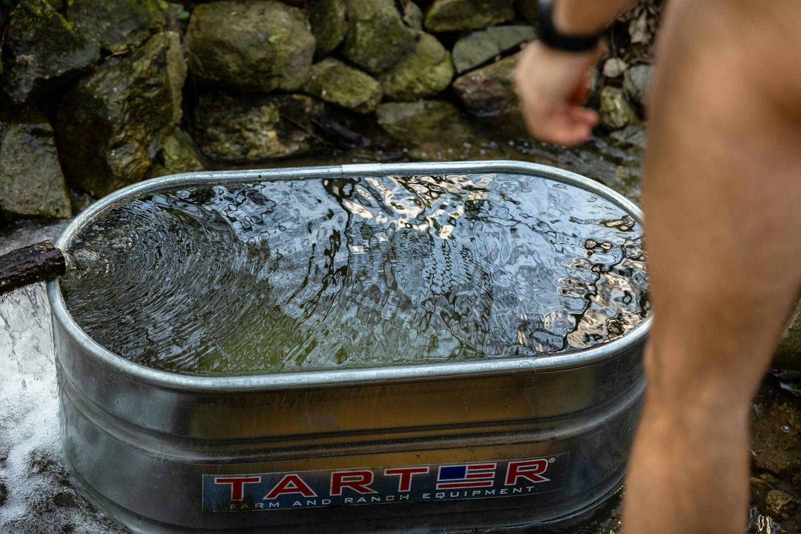 Homme debout à côté d'une grande baignoire métallique remplie d'eau froide, illustrant la taille d'un bain froid