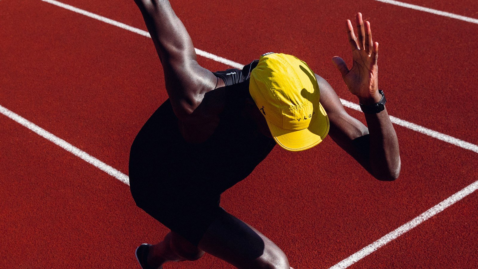 Sprinteur en casquette jaune au départ sur une piste rouge