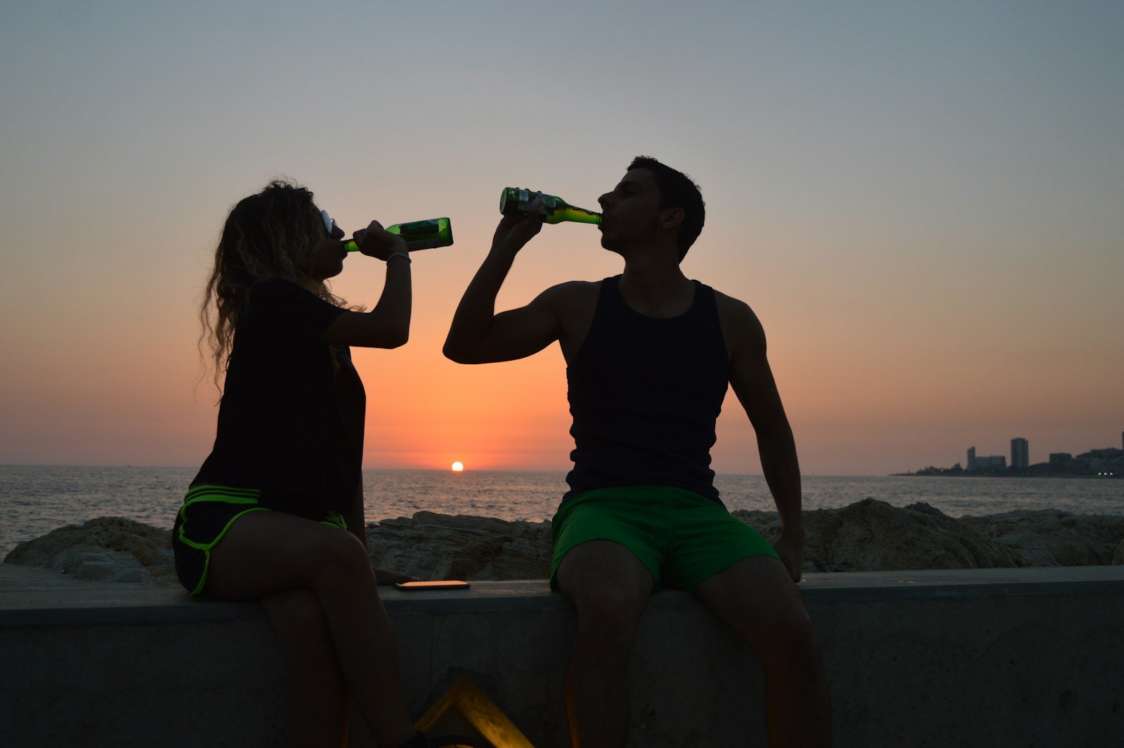 Deux sportifs en tenue de course buvant une bière au coucher du soleil après l'effort