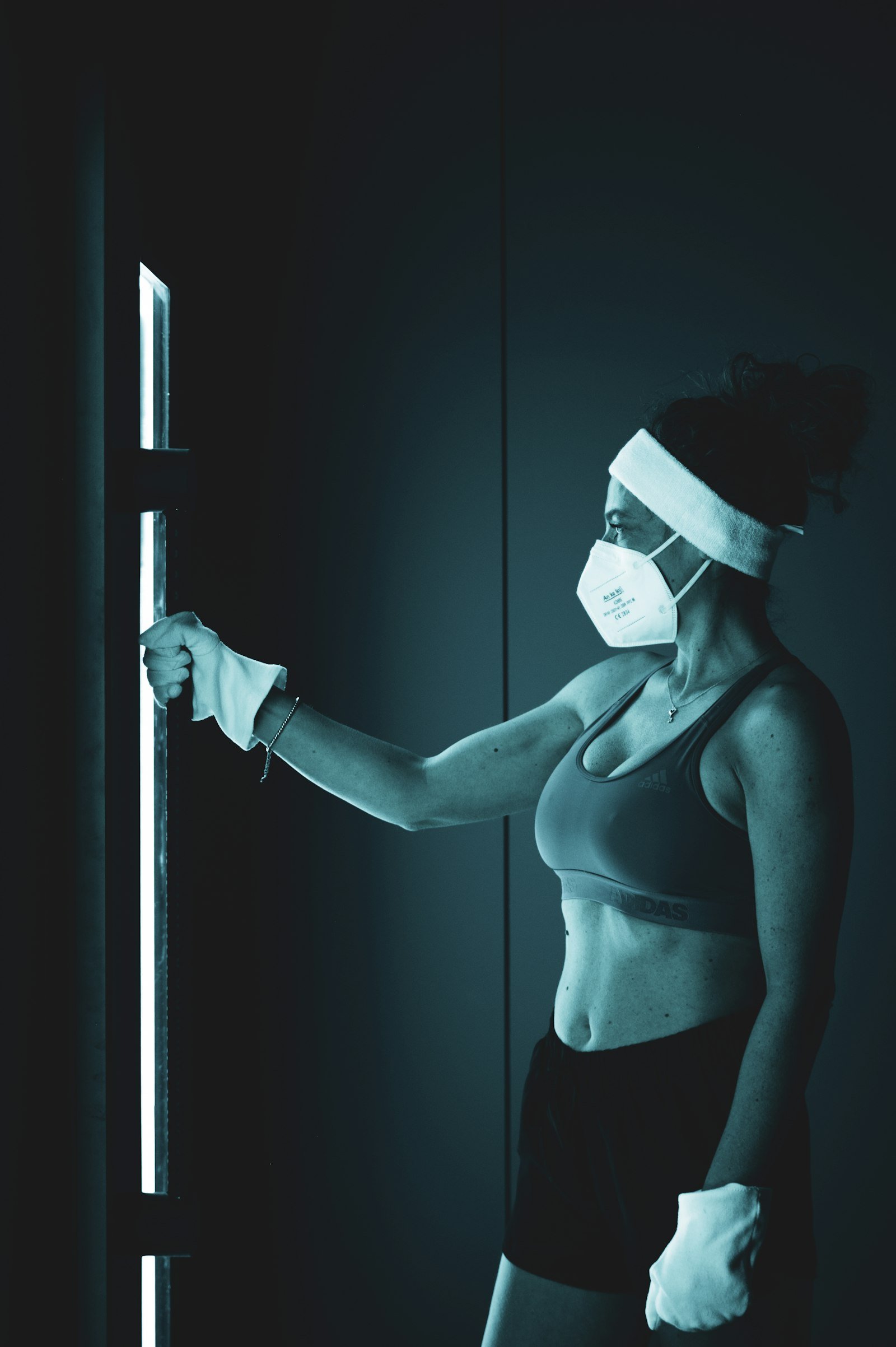 Femme en tenue de sport avec gants, bandeau et masque, la main sur la porte d'une cabine de cryothérapie