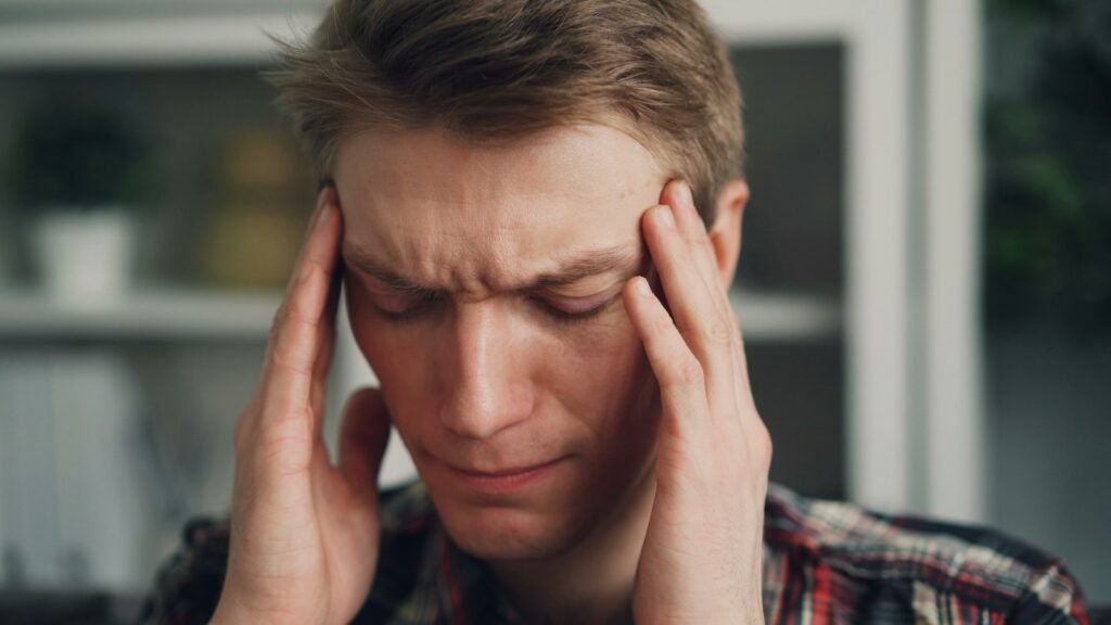 Homme les yeux fermés se tenant les tempes à deux mains, en pleine migraine