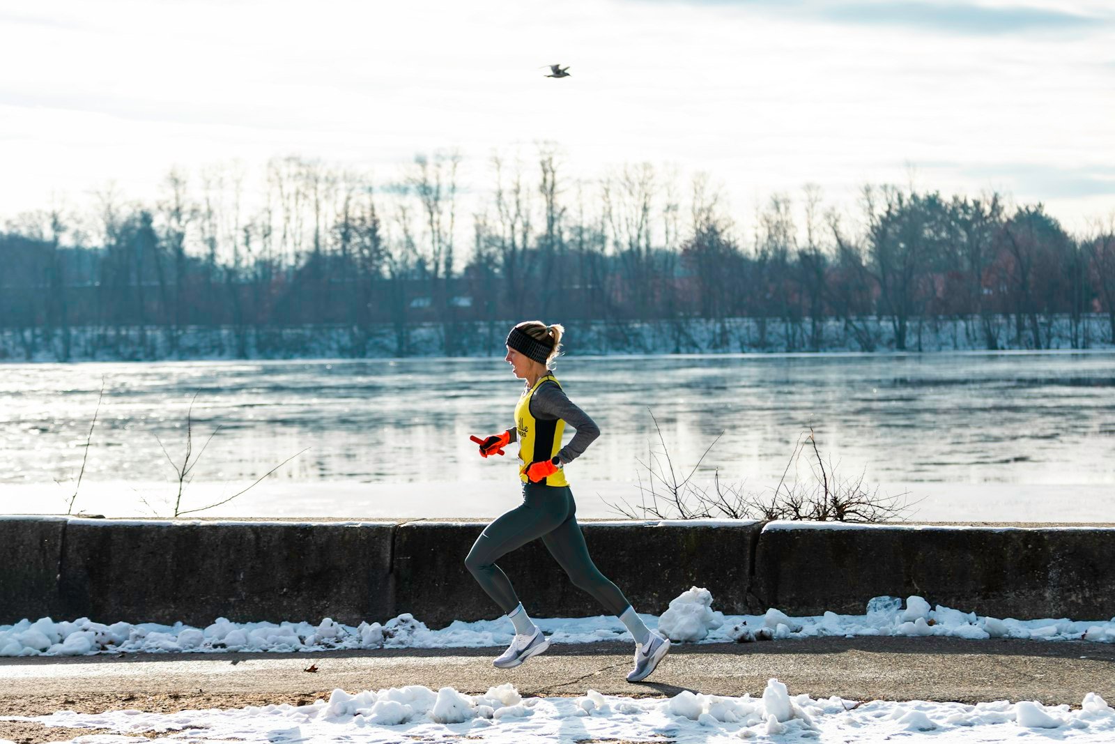 Coureuse en tenue d'hiver le long d'une rivière gelée, sous un ciel froid