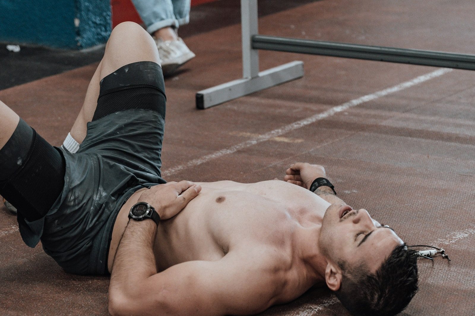 Sportif allongé au sol d'une salle de musculation, à bout de souffle à côté d'une barre chargée