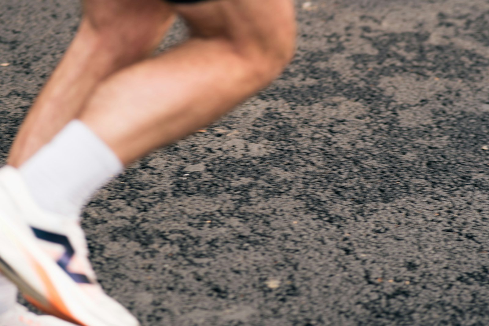 Jambes d'un coureur en pleine foulée sur l'asphalte, mollets et tendons d'Achille sollicités