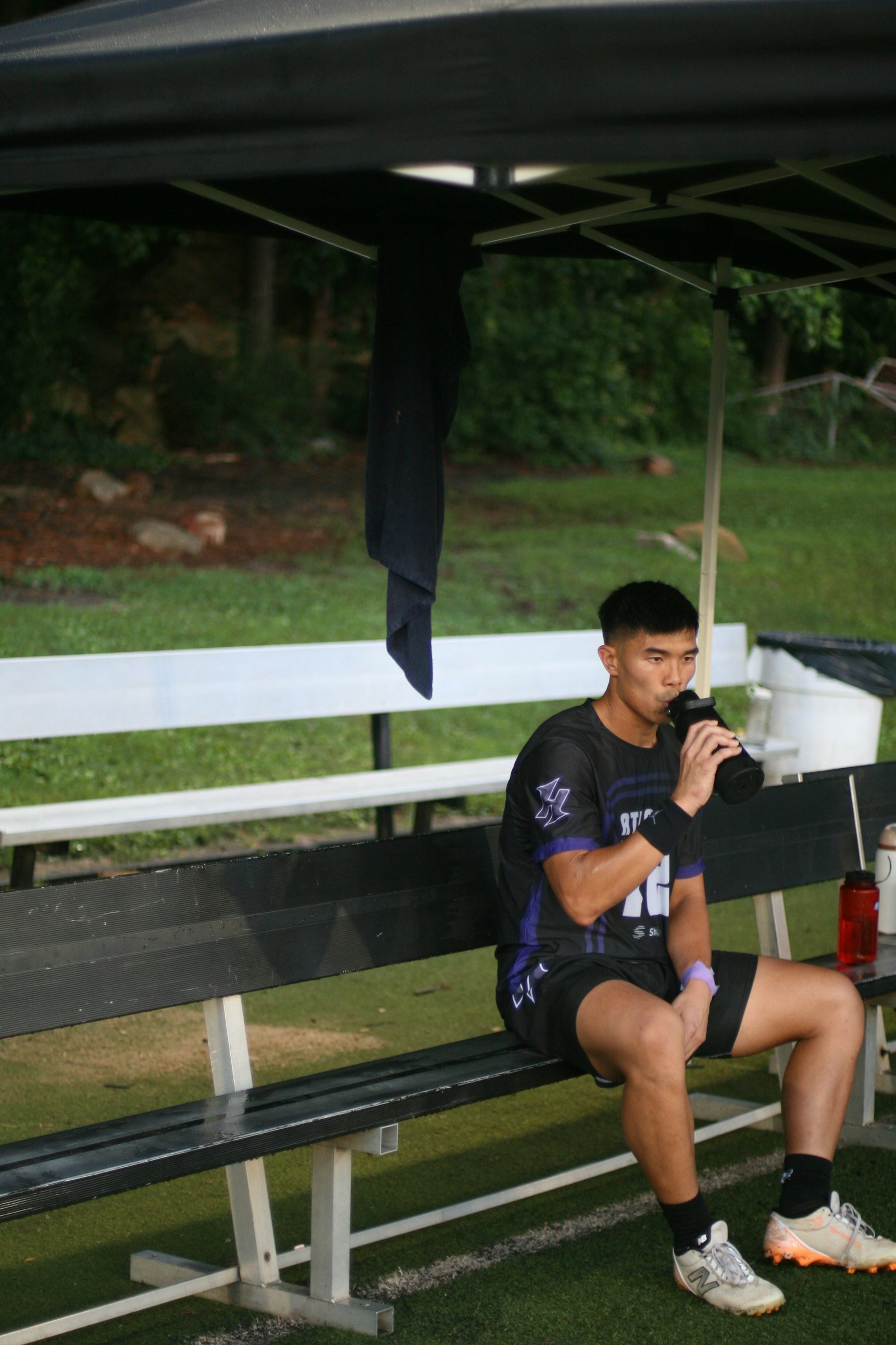 Sportif en maillot noir assis sur un banc, une gourde à la main